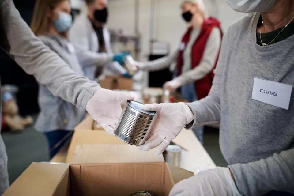 Close-up of people wearing white gloves and Covid-19 masks exchanging unlabeled can of food at food bank